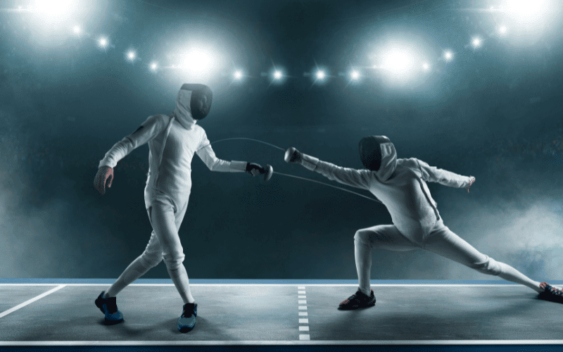 A fencer wearing protective gear practices footwork and sword techniques on a padded floor, with a coach observing and giving instructions